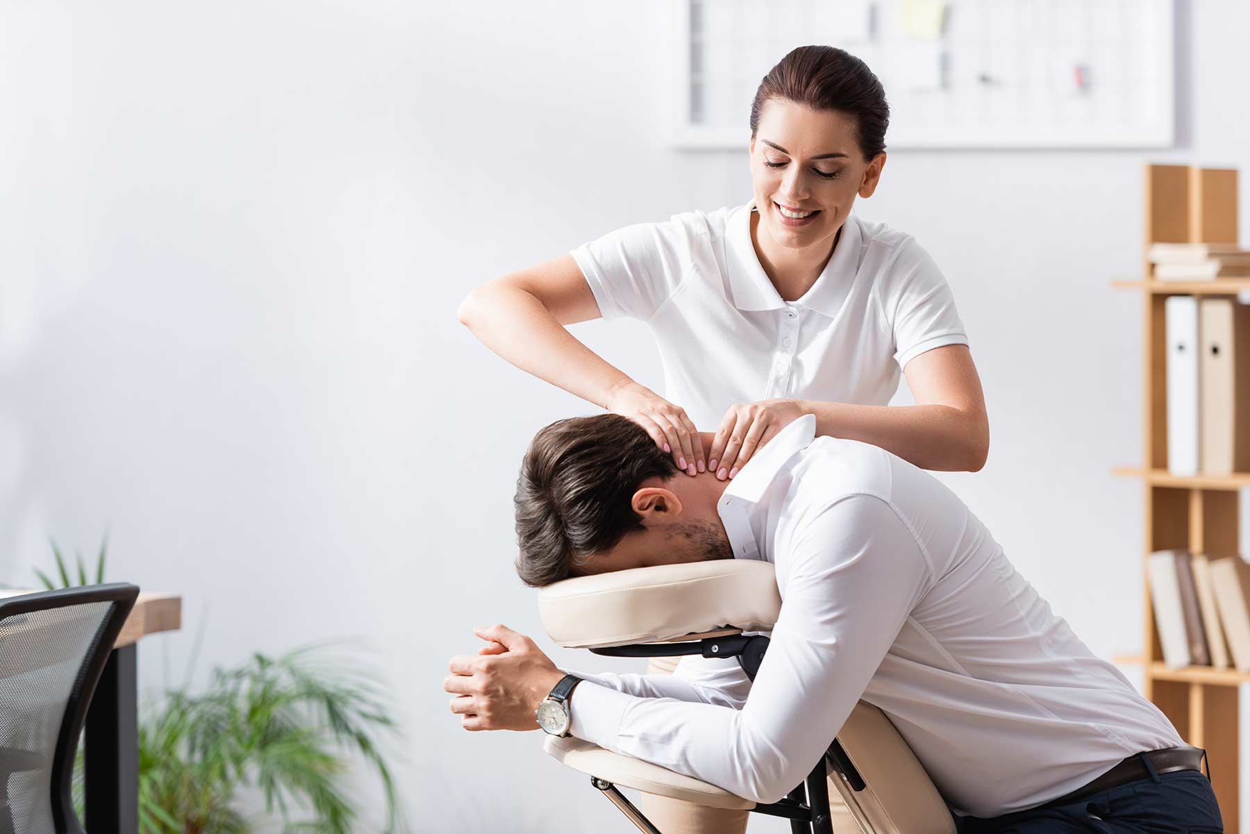 A massage therapist performing a chair massage to a client sitting upright