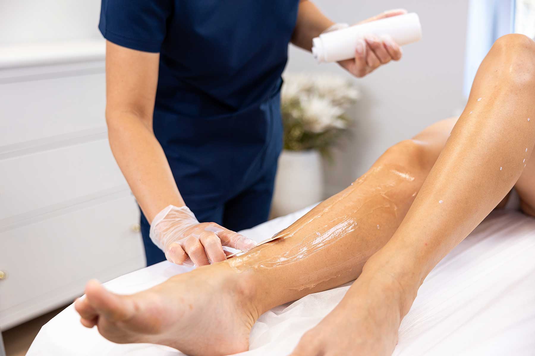 A beautician applying wax on a client's legs during a professional leg waxing treatment at a spa