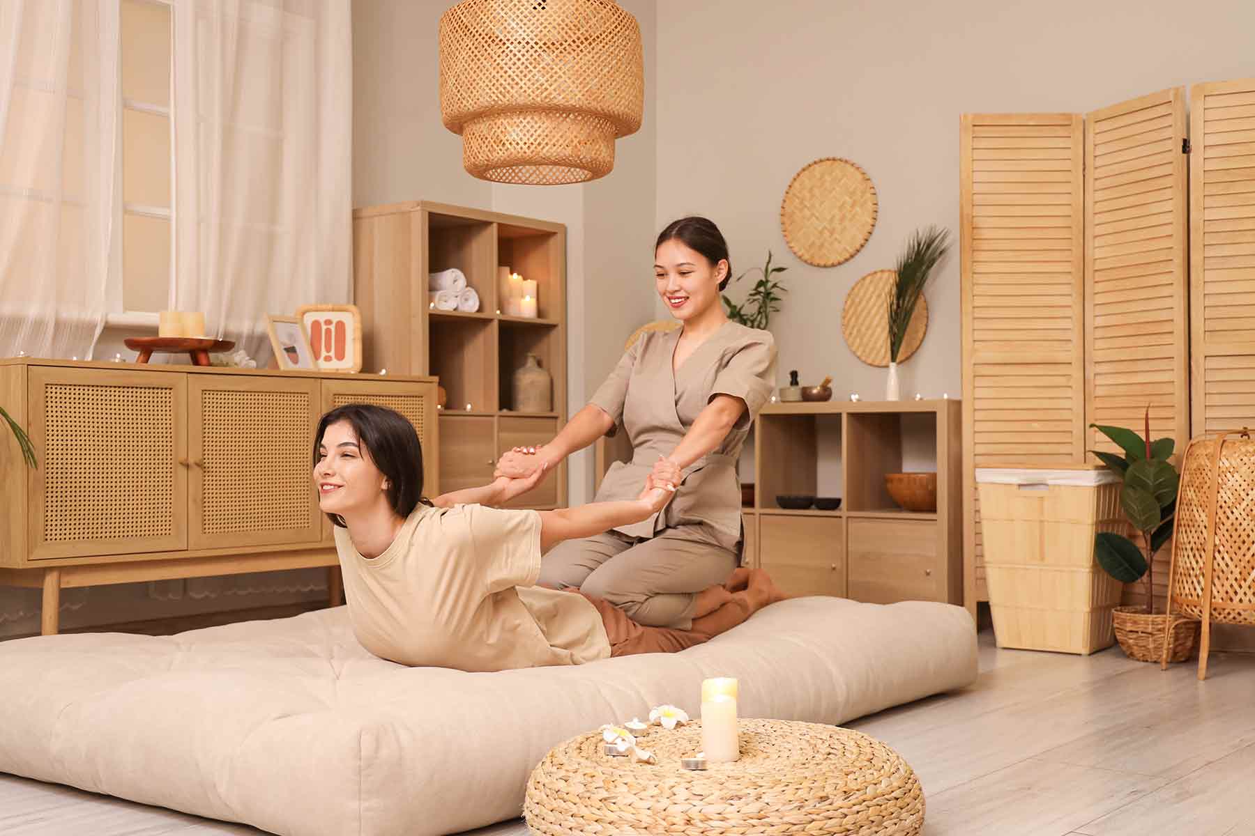 A massage therapist performing Thai massage by stretching a client’s arms